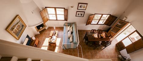 A spacious living area with a staircase, wooden furniture, and multiple windows allowing natural light.