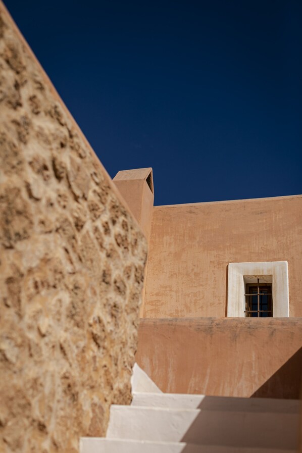 A staircase leading up to a building with a textured wall and a window with a grid pattern.