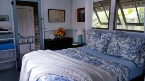 Quarto com cama, mesa de cabeceira, estante com livros, janela e porta.