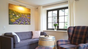 A living room with a sofa, a plaid armchair, a wooden barrel, and a window with curtains. - Lovingly furnished vacation apartment with sunny, quiet balcony facing the lavender (Freital)