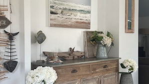 A room with a wooden dresser, a metal bucket with flowers, a framed picture, and a wall-mounted fish decoration. - House / Villa - Le Palais (Bangor)
