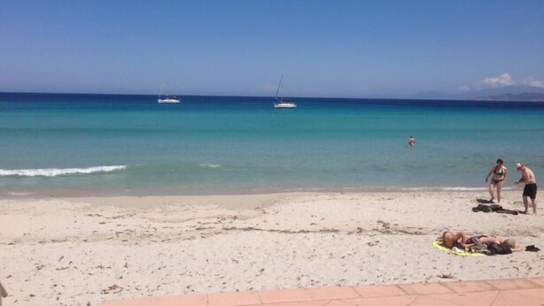 Ein Strand mit blauem Himmel, ruhiger See und einem Boot in der Ferne.
