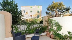 Ein Balkon mit zwei Korbstühlen, einem kleinen Tisch und mehreren Blumentöpfen.