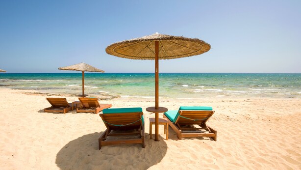 Una spiaggia con lettini di legno e ombrelloni di paglia.