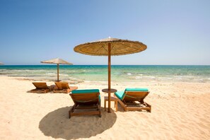 Une plage avec des chaises longues en bois et des parasols en chaume.