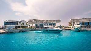 Una marina con un grande yacht ormeggiato al centro, circondata da edifici moderni con ampie finestre e una zona coperta.