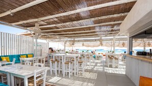 Area esterna con tavoli e sedie bianche, un bar e vista sul mare.