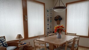 Un coin repas avec une table et des chaises en bois, un vase de fleurs et une horloge fixée au mur.
