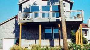 Une maison à deux étages avec un balcon au dernier étage, entourée de végétation.