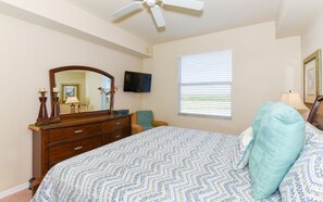 Een slaapkamer met een bed, dressoir, televisie, raam en plafondventilator.