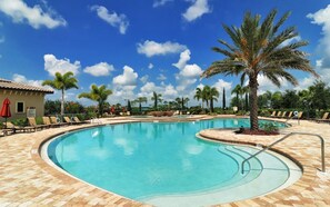 A swimming pool with lounge chairs and palm trees, surrounded by a tiled deck.