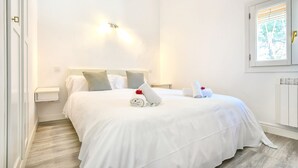 Ein ordentlich gemachtes Bett mit weißen Leinen und einer roten Rose, ein kleiner Nachttisch und ein Fenster mit Jalousien.