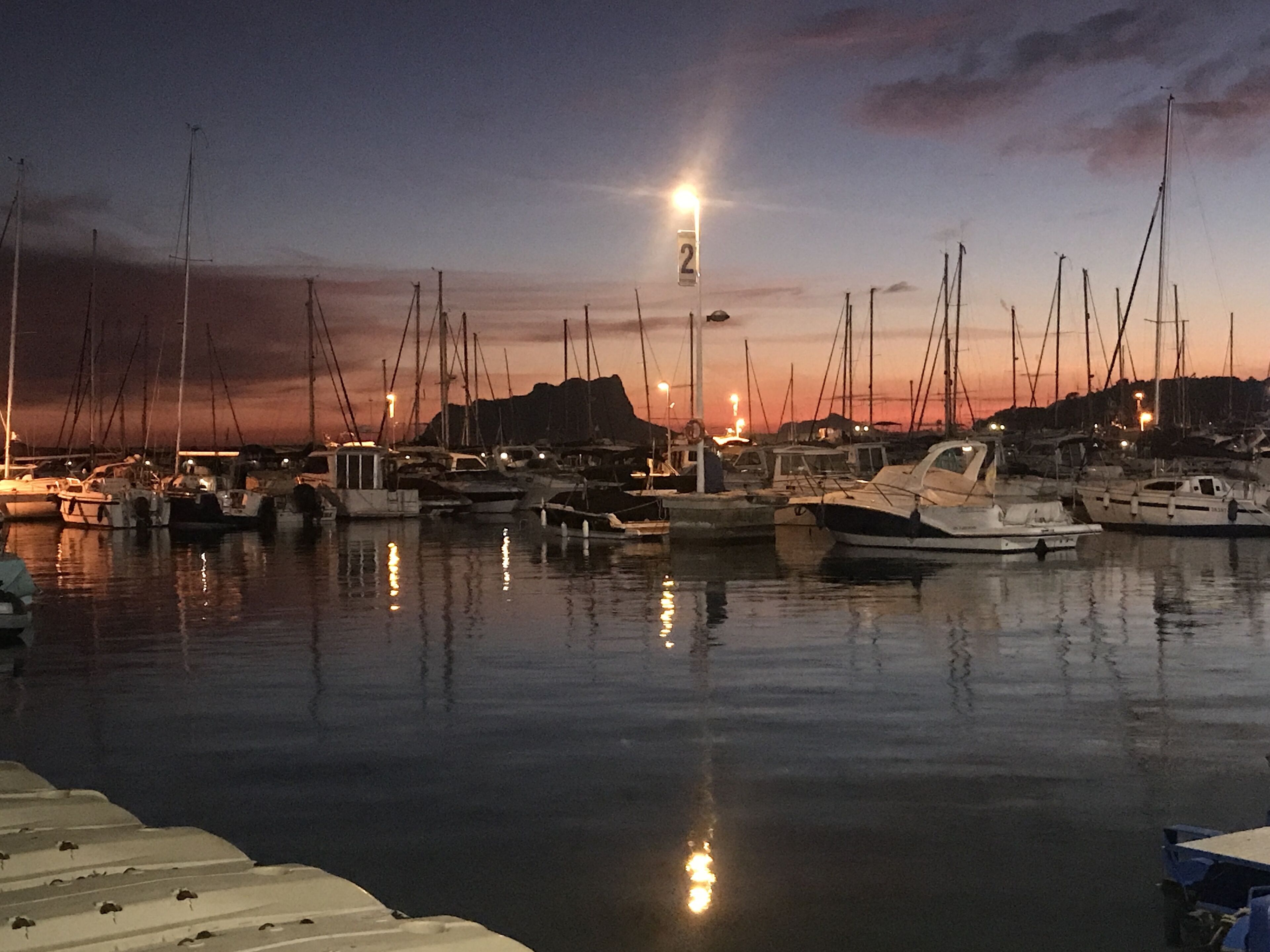 En marina i skumringen med tilkoblede både og en gadelampe.