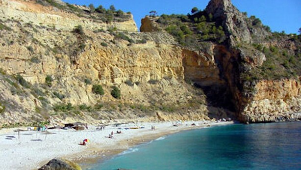 Ein Küstenstrand mit klarem türkisblauem Wasser, felsigen Klippen und einem sandigen Ufer.