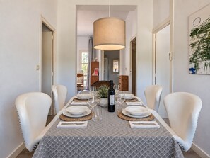 A dining area with a table set for four, chairs, a hanging light fixture, and a painting on the wall.