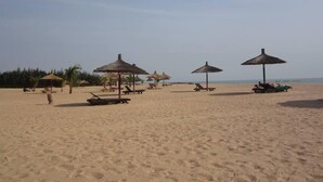 A beach with several thatched umbrellas and lounge chairs.