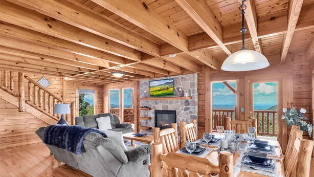 Interior de uma cabana de madeira com sala de estar, área de jantar e lareira de pedra.