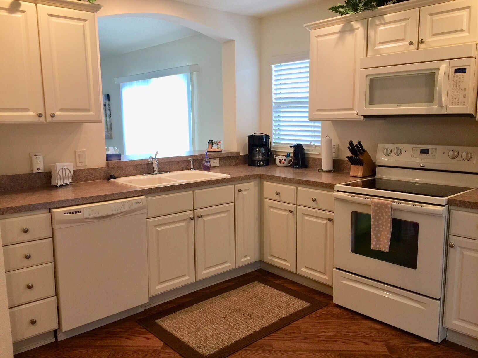 A kitchen with white cabinets, a double sink, a microwave, an oven, and a coffee maker.