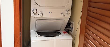 Una lavadora y secadora compactas en un lavadero pequeño con una puerta de madera y un enchufe a la vista.