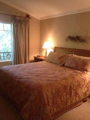 A bedroom with a large bed, a nightstand with a lamp, a window with curtains, and a wall decoration. - Del Mar Heights Hideway w/ BBQ, Pool access, 5min drive to Beaches, 20min to Zoo (San Diego)