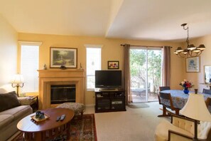 A living room with a fireplace, television, sofa, coffee table, and dining area with a table and chairs. - Del Mar Heights Hideway w/ BBQ, Pool access, 5min drive to Beaches, 20min to Zoo (San Diego)