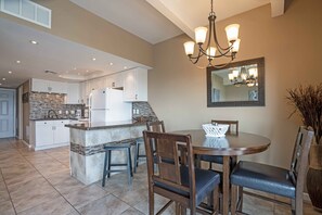 Una cocina moderna con armarios blancos, una isla de granito y un comedor con mesa y sillas de madera.