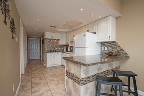 Una cocina con armarios blancos, encimera de granito y una isla integrada con taburetes de bar.