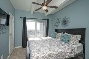 Ein Schlafzimmer mit Bett, Deckenventilator, Fenster mit Vorhängen und Wandbildern.
