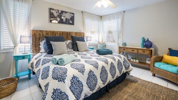 A bedroom with a bed, a ceiling fan, a world map on the wall, and a wicker sofa. - Sunny 3BR/3BA Home.  8 Houses from Beach.  Two Master Suites. (Holmes Beach)