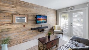 A living room with a wooden wall, a flat-screen TV mounted above a fireplace, a comfortable sofa, and a chair. - Sunny 3BR/3BA Home.  8 Houses from Beach.  Two Master Suites. (Holmes Beach)