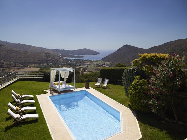 A pool area with a bed, lounge chairs, and a view of the sea.
