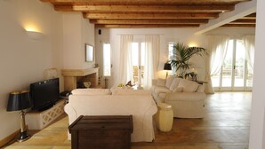 Een ruime woonkamer met houten plafond, een zithoek, een televisie en een salontafel.