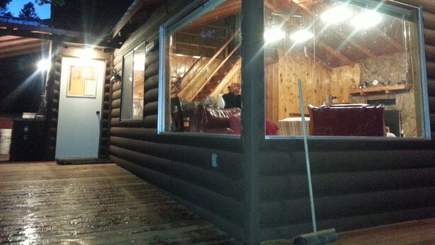 Una cabaña de madera con fachada de vidrio, interior de madera y una escalera visible.