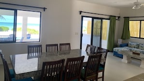 A dining area with a large table and chairs, a sofa, and a view of the ocean through large windows. - BEROCO Front Beach House Yucatan Wi-Fi, Pool, Smart Tv (Uaymitun)