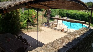 Ein überdachter Außenbereich mit Pool, Steinwänden und einem Tisch mit Stühlen.