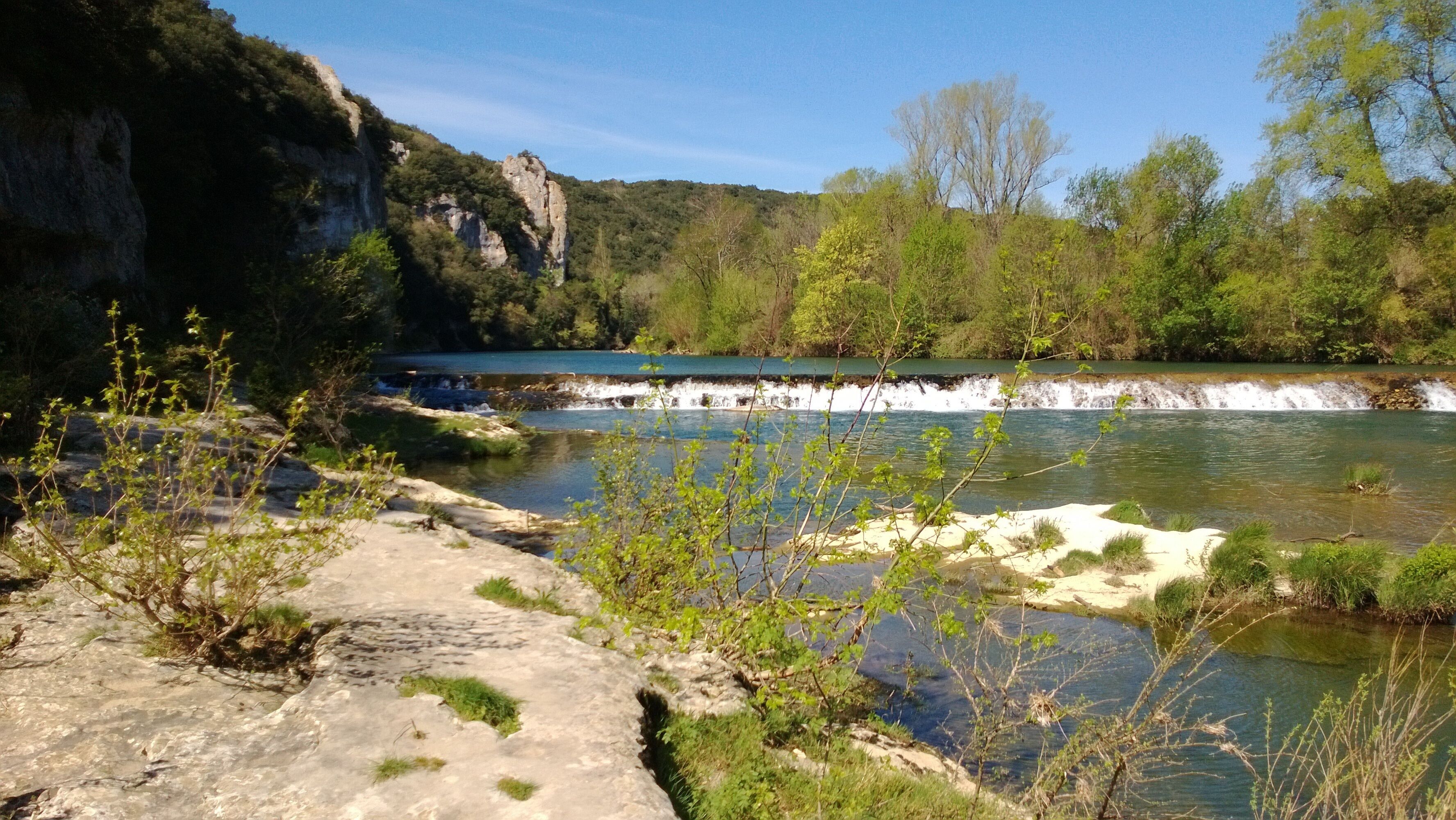 Un río con cascada, rodeado de vegetación y acantilados rocosos.