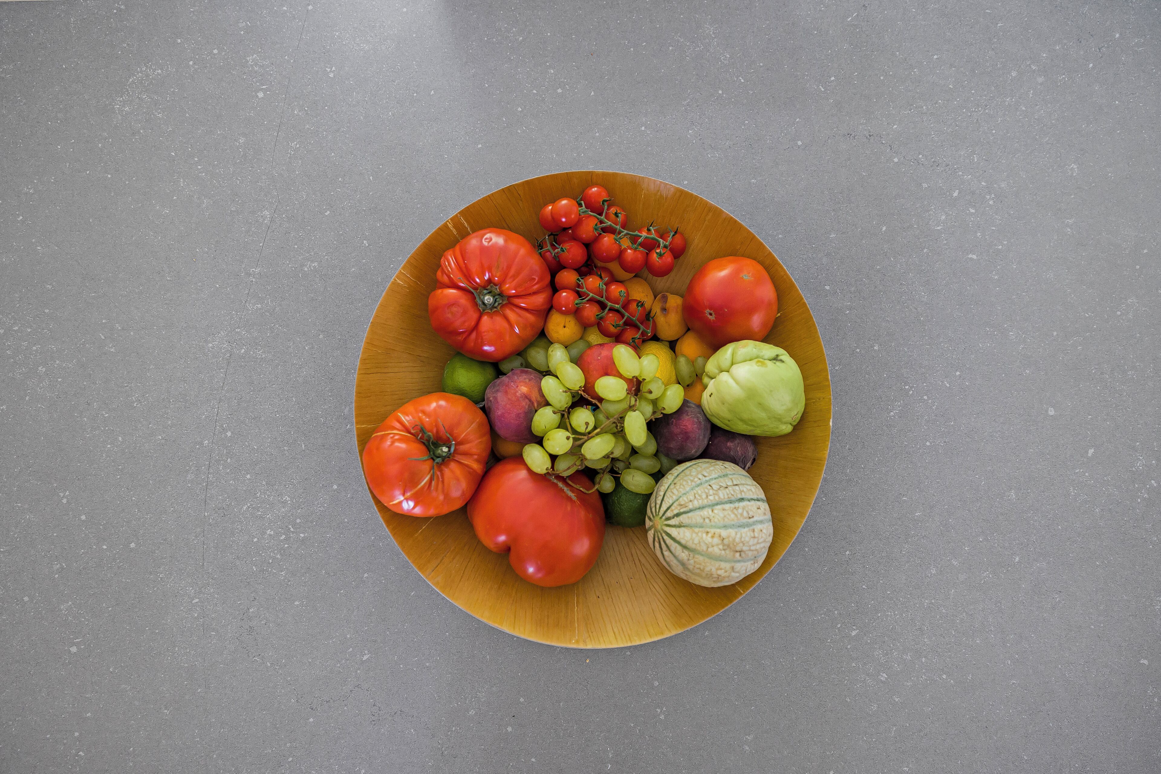 Een houten bord met verschillende soorten fruit en groenten op een grijze ondergrond.
