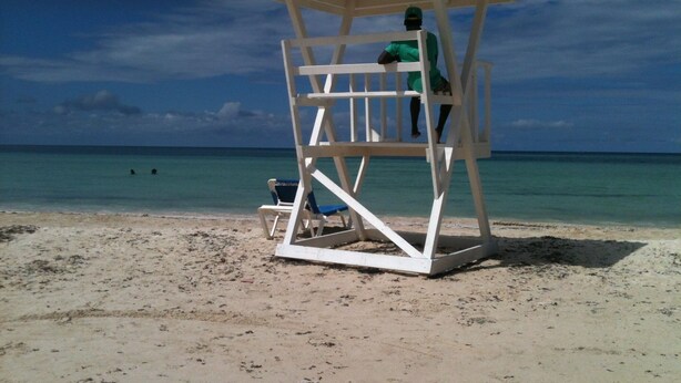 Une tour de surveillance sur une plage, avec une eau d’un bleu limpide et un ciel partiellement nuageux.