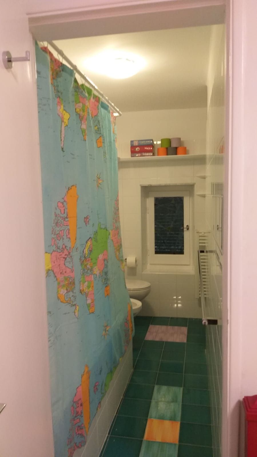 A bathroom with a shower curtain featuring a world map, a toilet, and a small window.