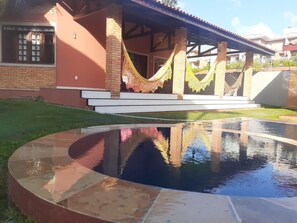 A pool with a reflection, a covered patio area with steps, and a building with a brick facade.