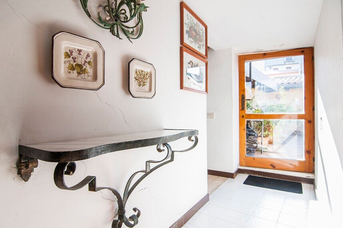 A hallway with a wooden door, a black metal shelf, and three framed artworks on the wall.