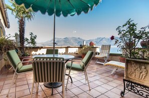 Una terraza con mesa y sillas, plantas en macetas y vistas a montañas.