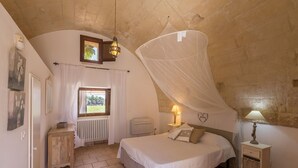 Une chambre à coucher comprenant un lit, des lampes de chevet, un radiateur, une fenêtre avec des rideaux et un radiateur fixé au mur.