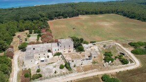 Une vue aérienne d’un ensemble de bâtiments historiques comprenant plusieurs structures, entouré de vastes champs et de forêts denses, et dominant une côte.