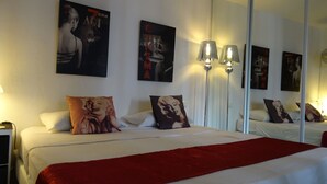 Hotellihuone, jossa on suuri sänky, kaksi seinälle asennettua lamppua ja julisteita seinillä.