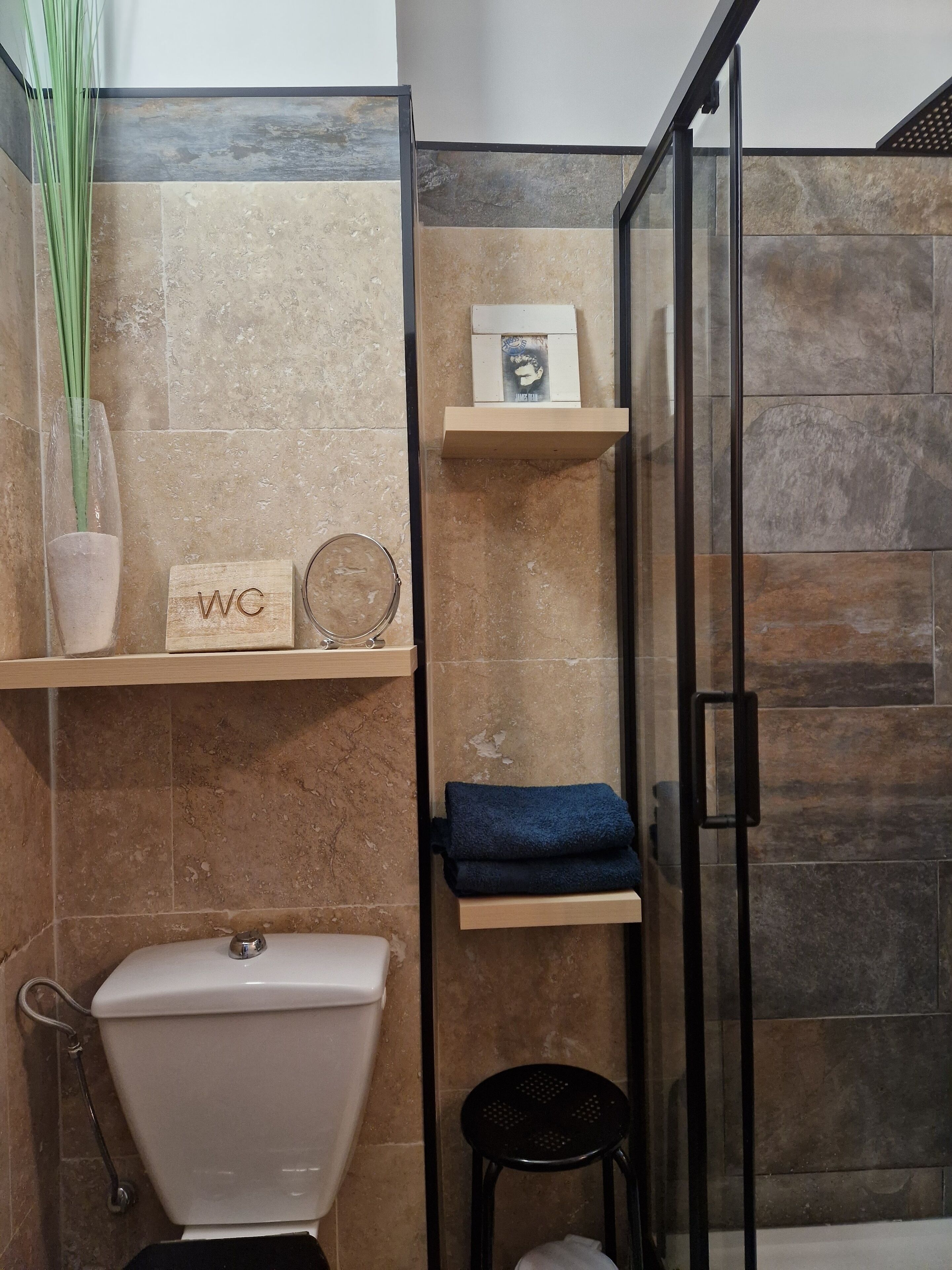 Un bagno con il water, una doccia e un lavandino. Si vedono scaffali con articoli da toilette e un asciugamano.