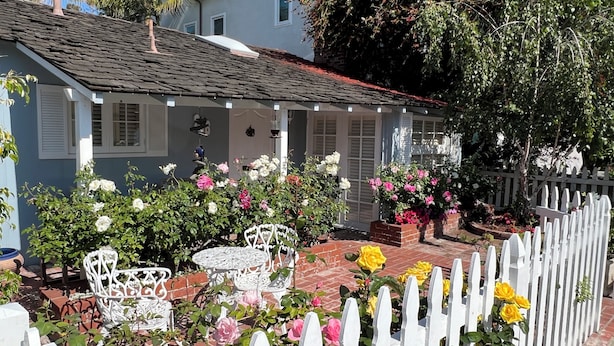 Een huis met veranda, witte picket fence en een tuin met diverse bloemen en witte tuinmeubels.