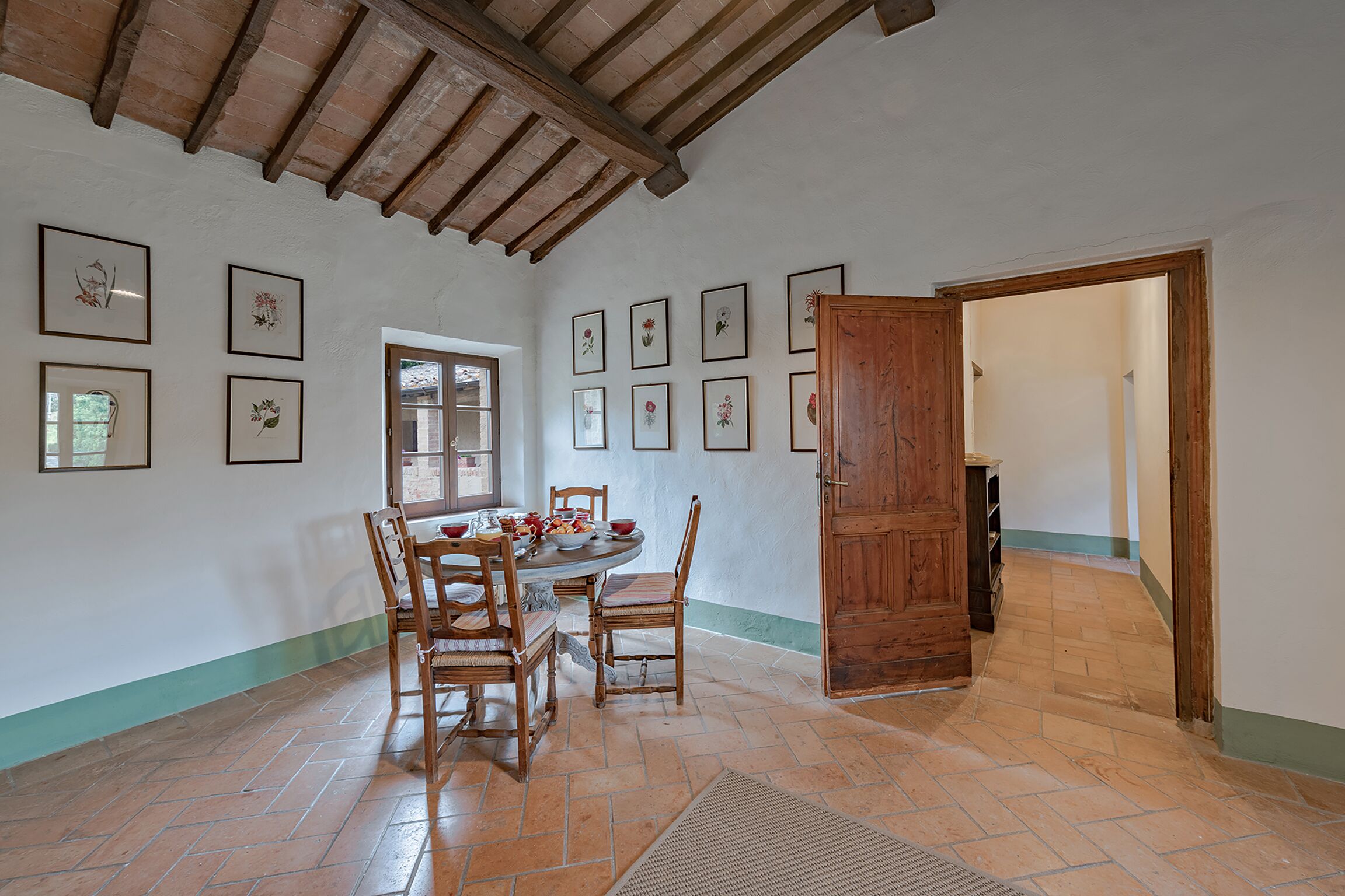 Un comedor con mesa y sillas de madera, rodeado de cuadros con motivos florales en las paredes.