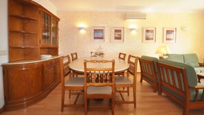 Uma sala de jantar com mesa e cadeiras de madeira, um armário e um sofá.