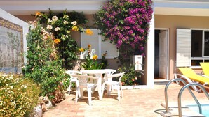 Um pátio com piscina, cadeiras de plástico branco e uma mesa.